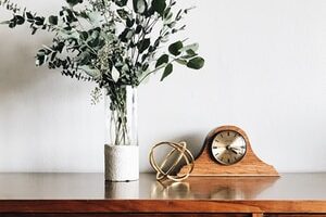 brown wooden framed analog mantle clock near gray petaled flower centerpiece